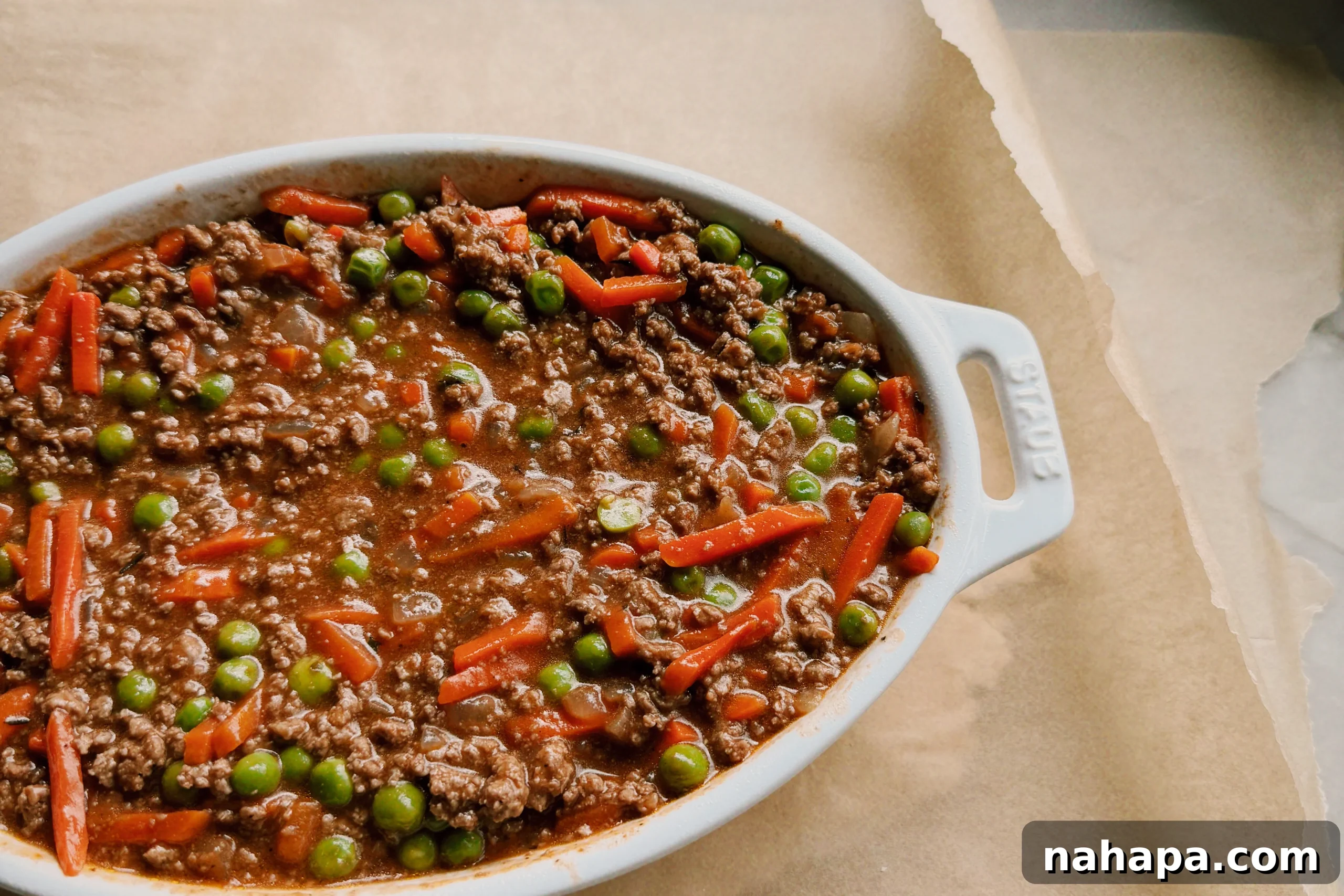 A white staub pan with the ground beef mixture filling it sitting on top of dough and parchment paper.