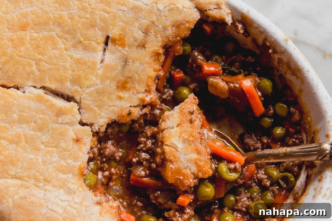 A close up of the cooked beef pot pie with a silver spoon taking a serving out of the container. 