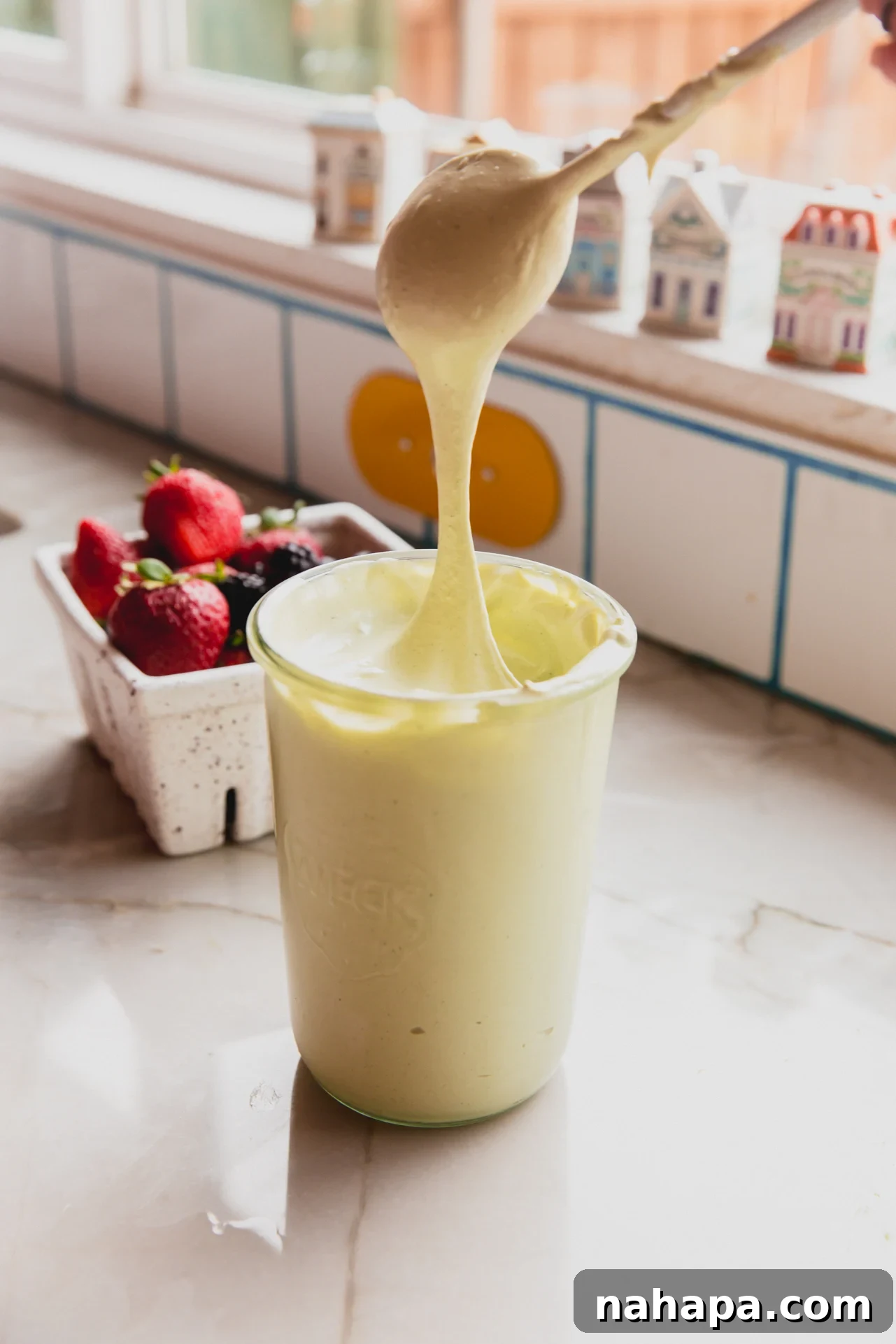 Matcha marshmallow fluff in a jar with a spoon dipping in and pulling up the marshmallow cream. The vibrant green color is inviting.