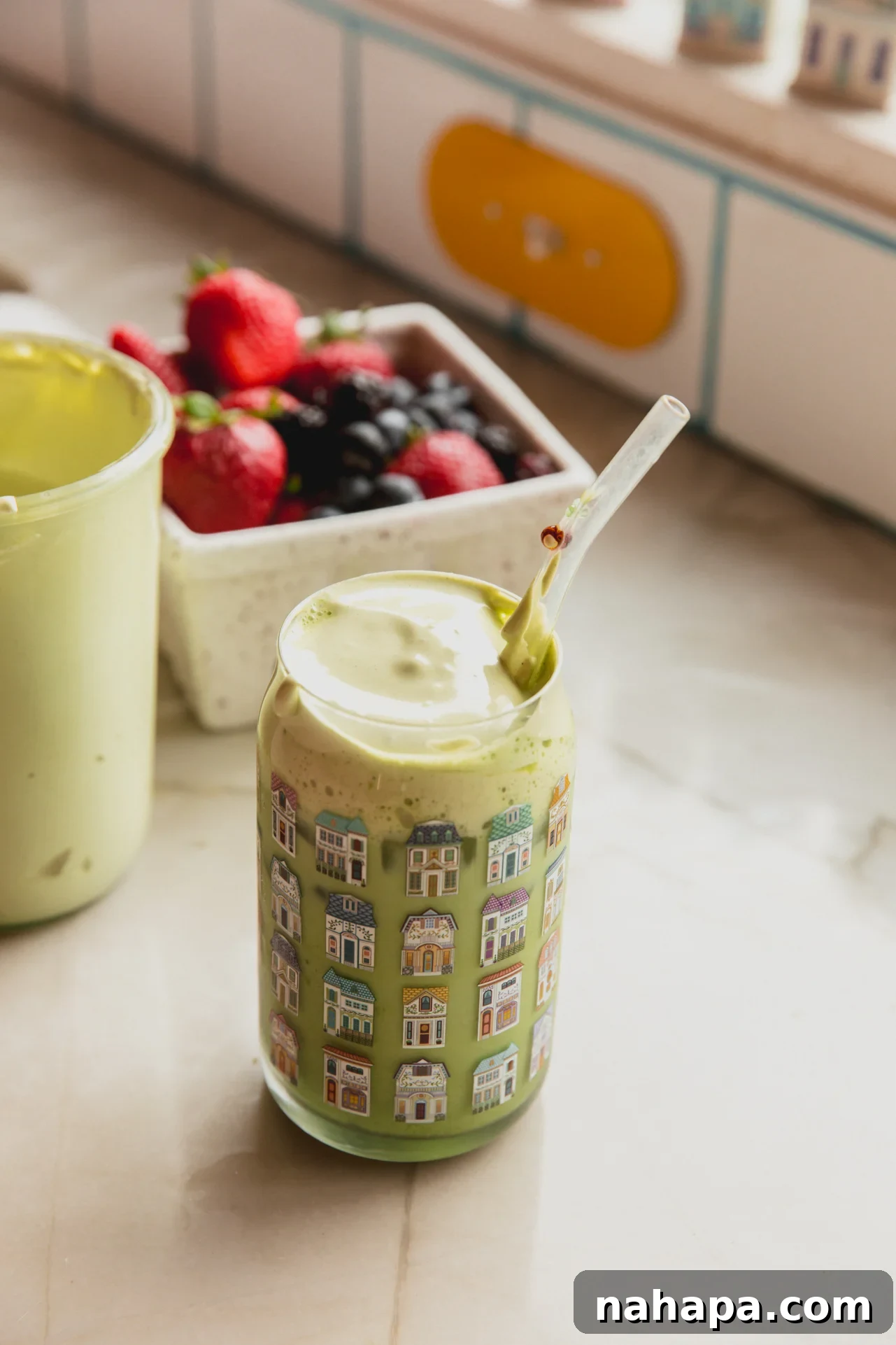 Iced matcha latte with marshmallow fluff on top and strawberries in the background, creating a refreshing and inviting scene.