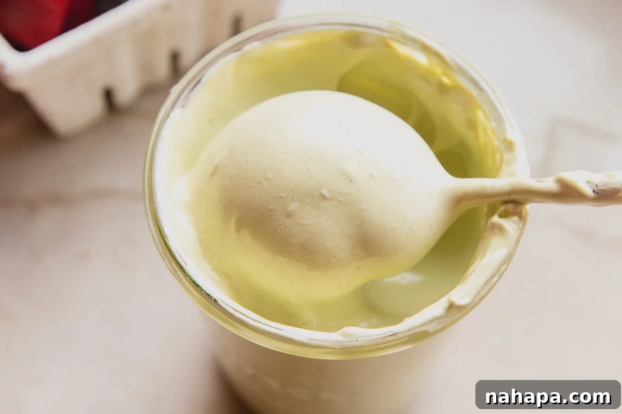 A glass jar filled with vibrant green matcha marshmallow fluff, with a spoon taking a generous spoonful out of it, highlighting its fluffy texture.