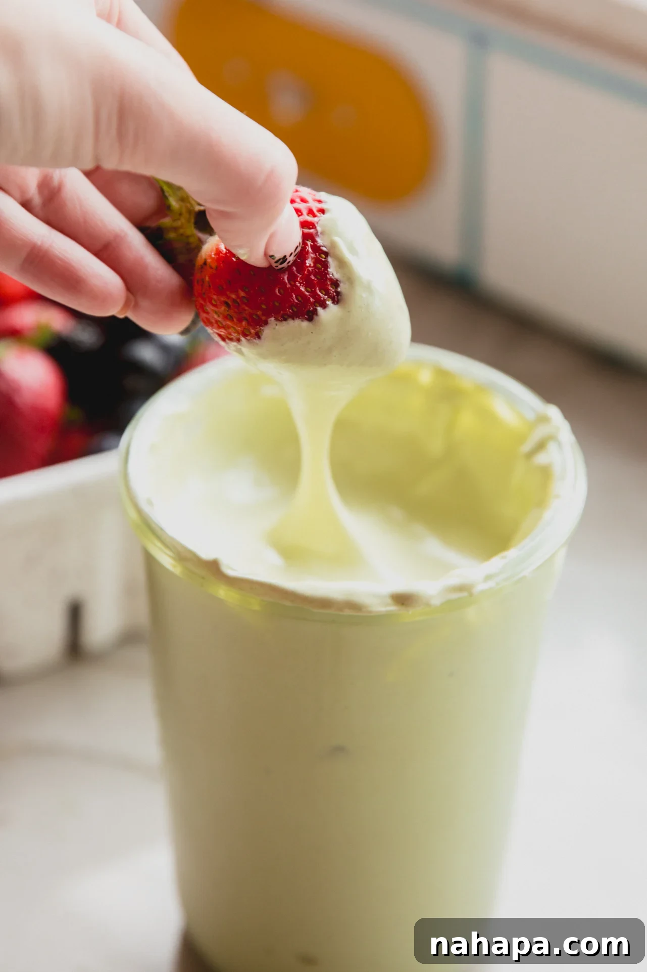 Matcha marshmallow fluff with a strawberry dipping in, showcasing its appealing texture and vibrant color.