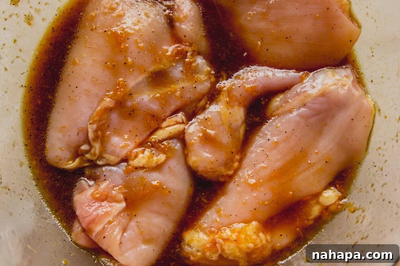 Sunshine-Spiced Chicken and Rice Broth 4 A clear glass bowl with chicken thighs marinating in a golden-hued mixture.