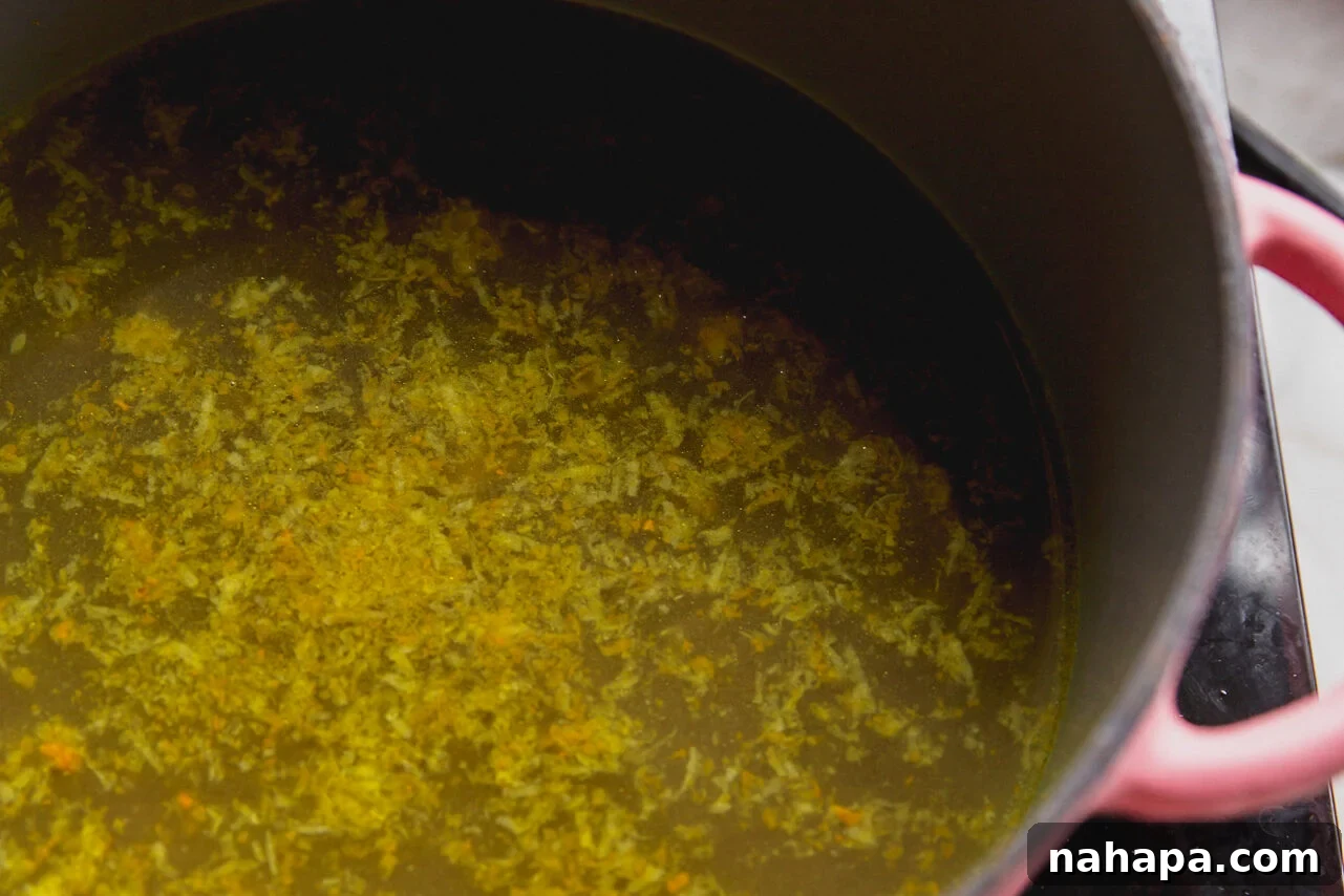 Sunshine-Spiced Chicken and Rice Broth 5 A pink pot with a golden turmeric broth simmering gently on the stovetop.
