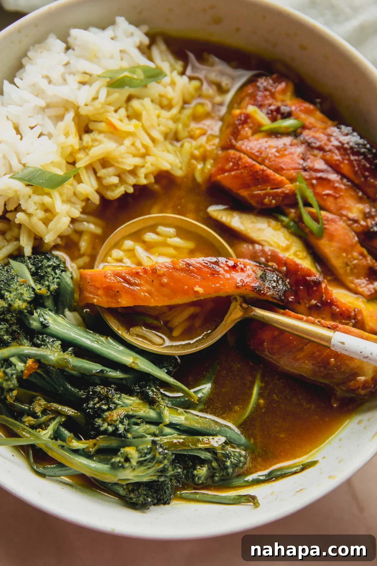 Sunshine-Spiced Chicken and Rice Broth 8 A white bowl of brothy turmeric chicken and rice, with a spoon gently lifting a piece of chicken, rice, and broth, showcasing the dish's inviting texture.