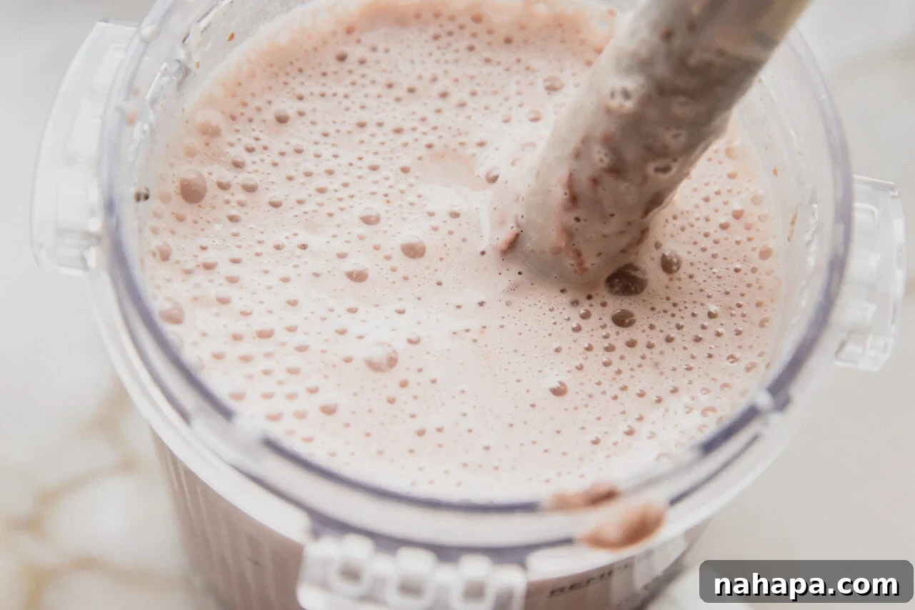 All Ninja Creami ingredients (yogurt, maple syrup, almond milk, chia seeds, protein powder) being combined and blended with an immersion blender in the Ninja Creami pint container.