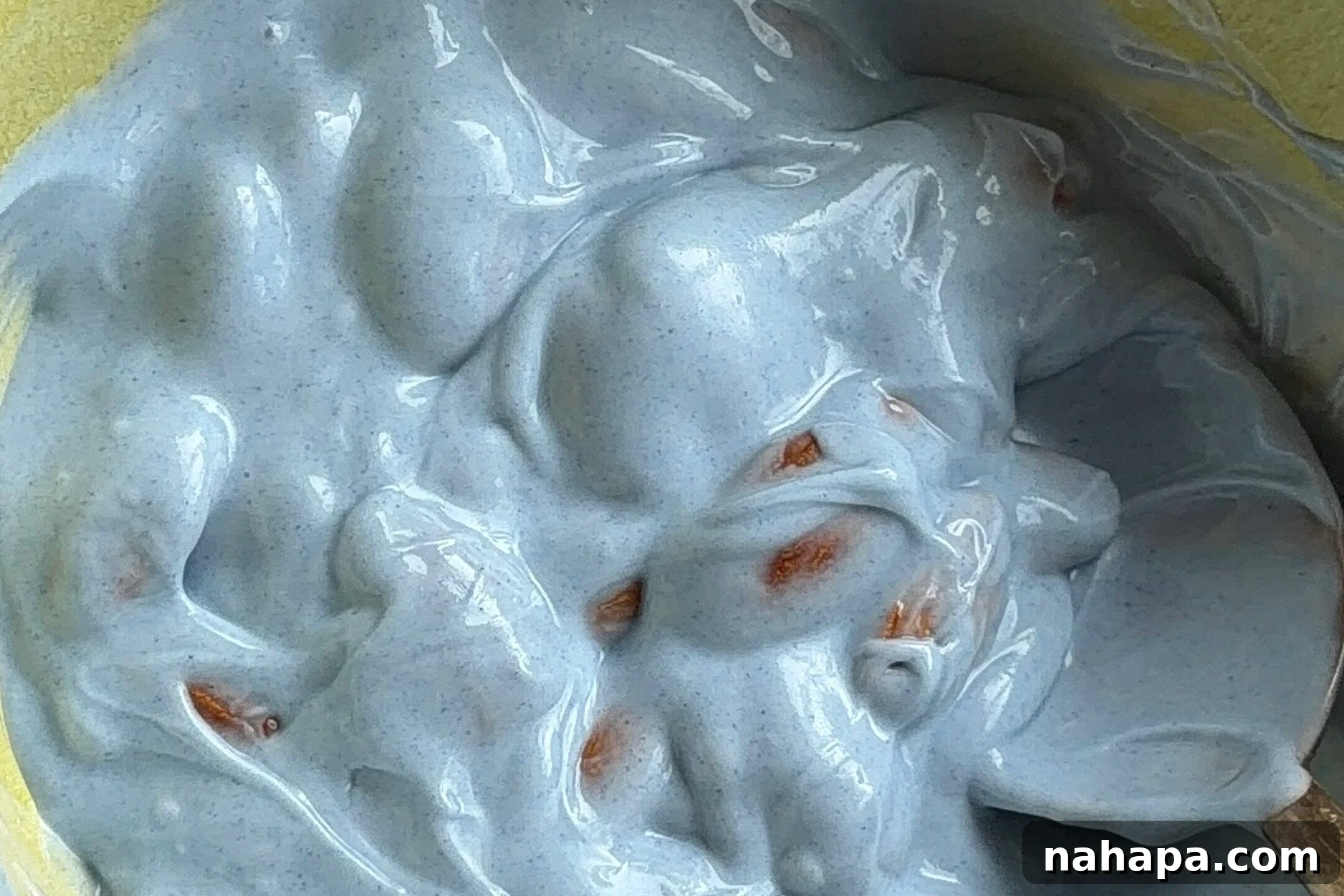 Almonds thoroughly mixed in a yellow bowl, completely coated in the blue chocolate and spirulina mixture, showing even coverage.