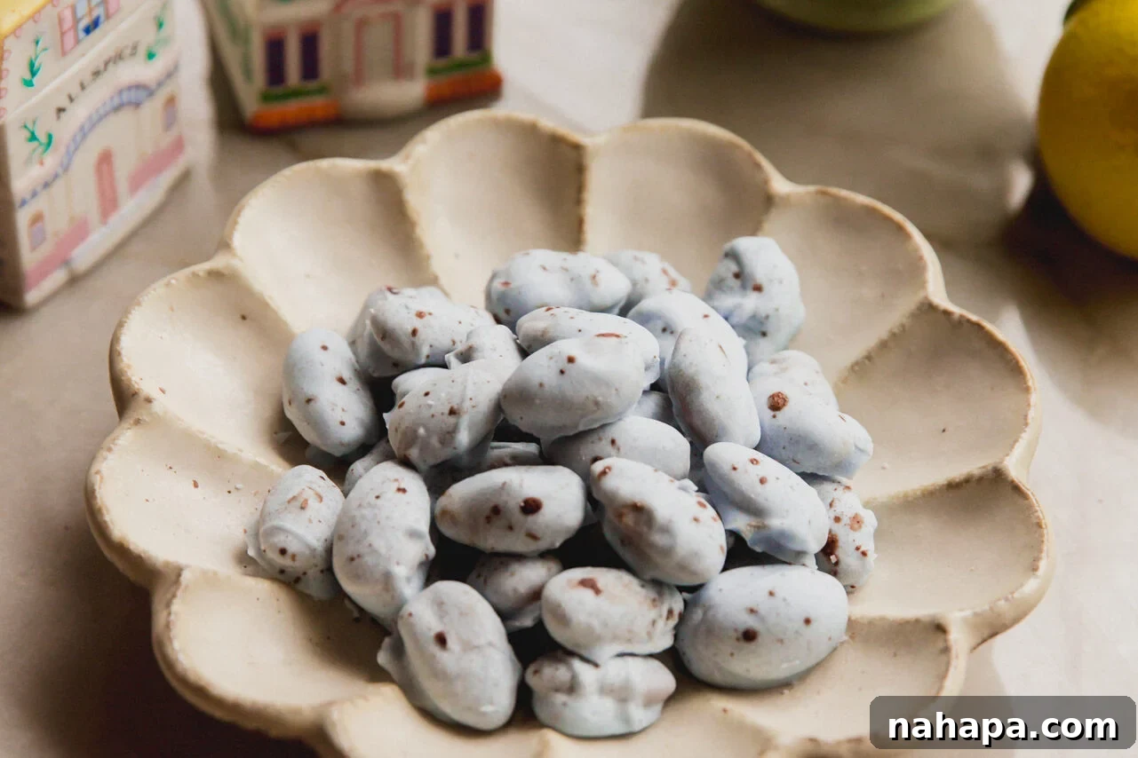 Finished blue chocolate covered almonds with brown speckles arranged in a bowl, set on a rustic table with spring decorations in the background.