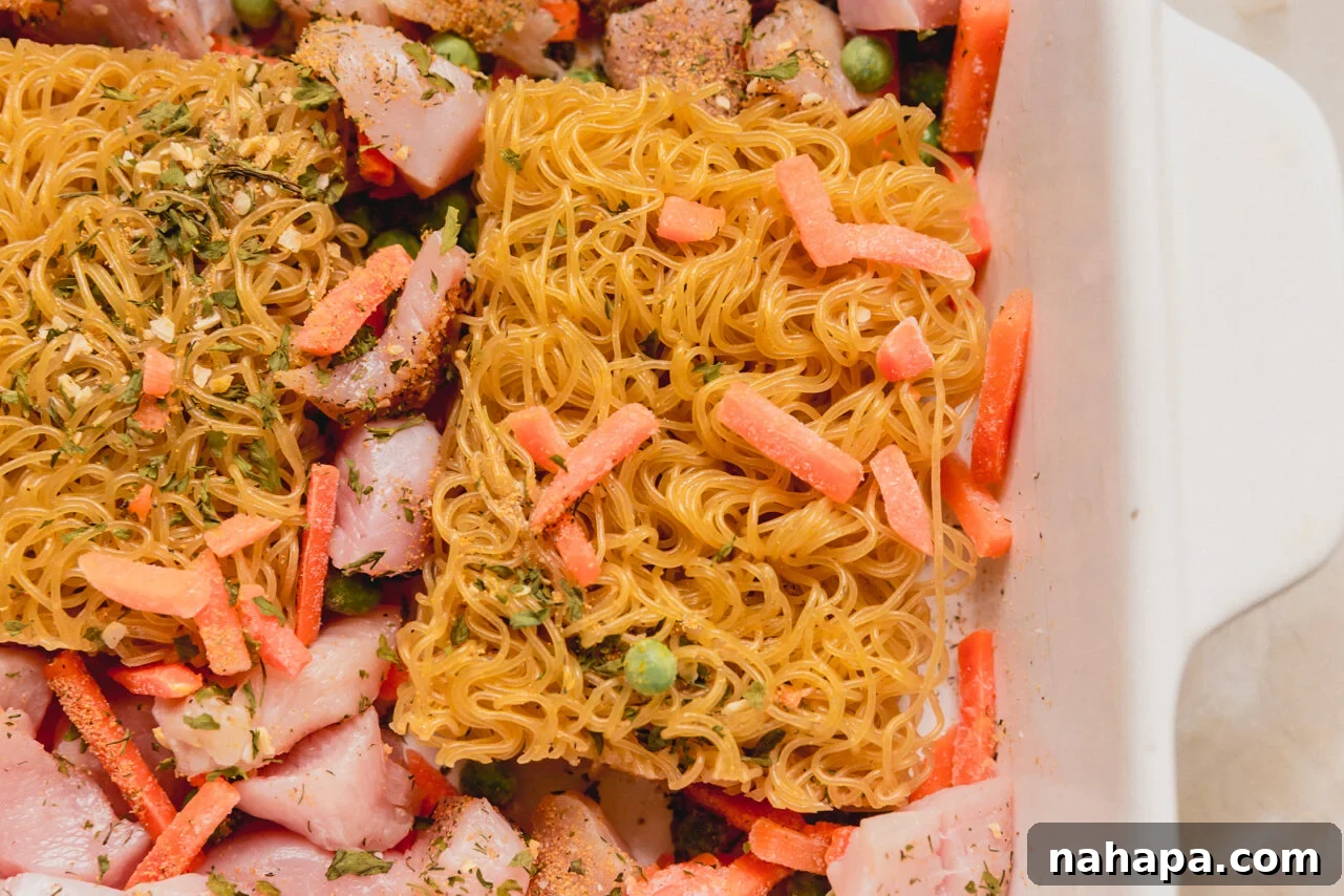 A casserole dish with ramen bricks, vegetables, and chicken in it before liquid is added.