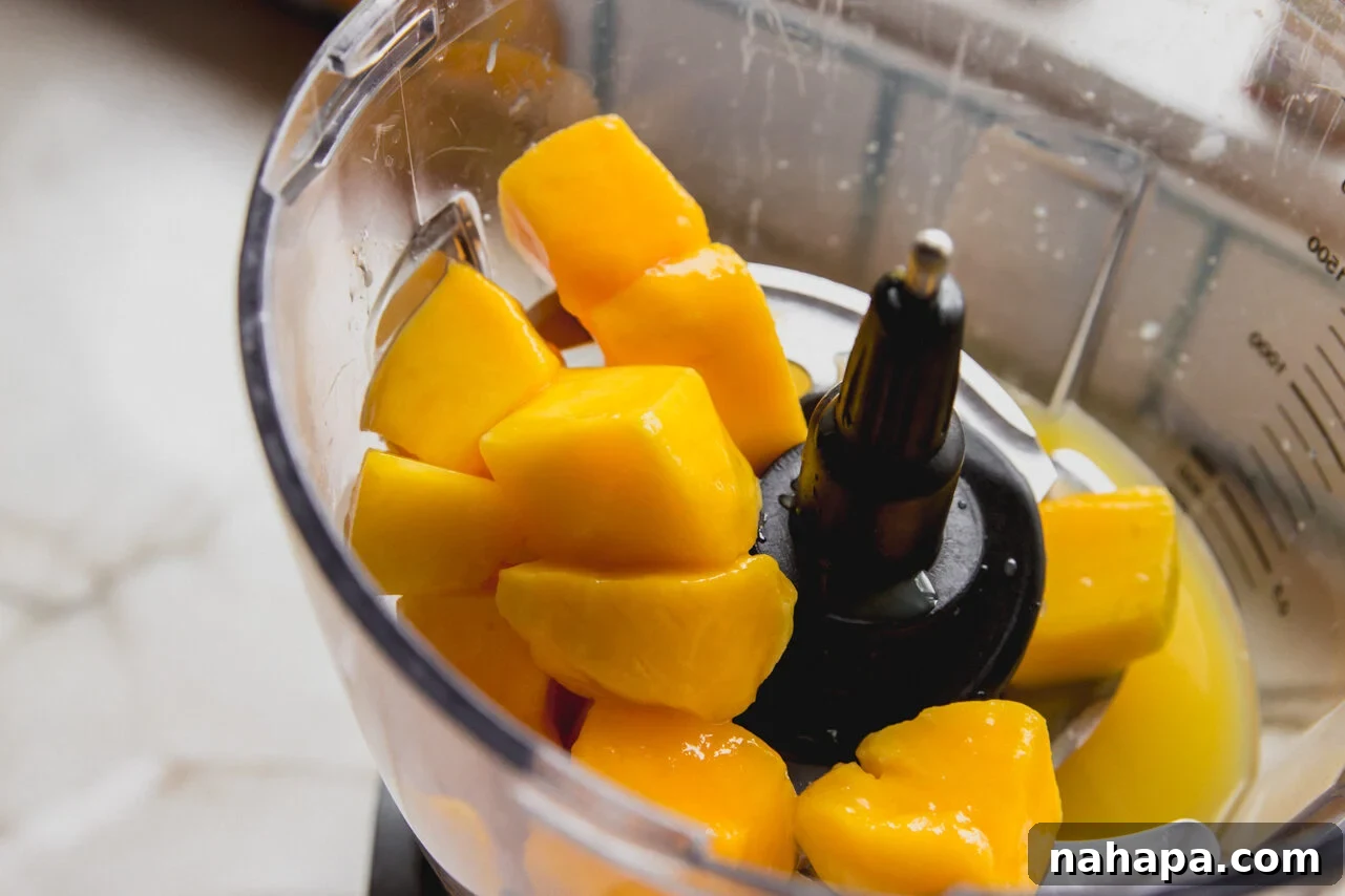 A food processor with mango and orange juice before blending.