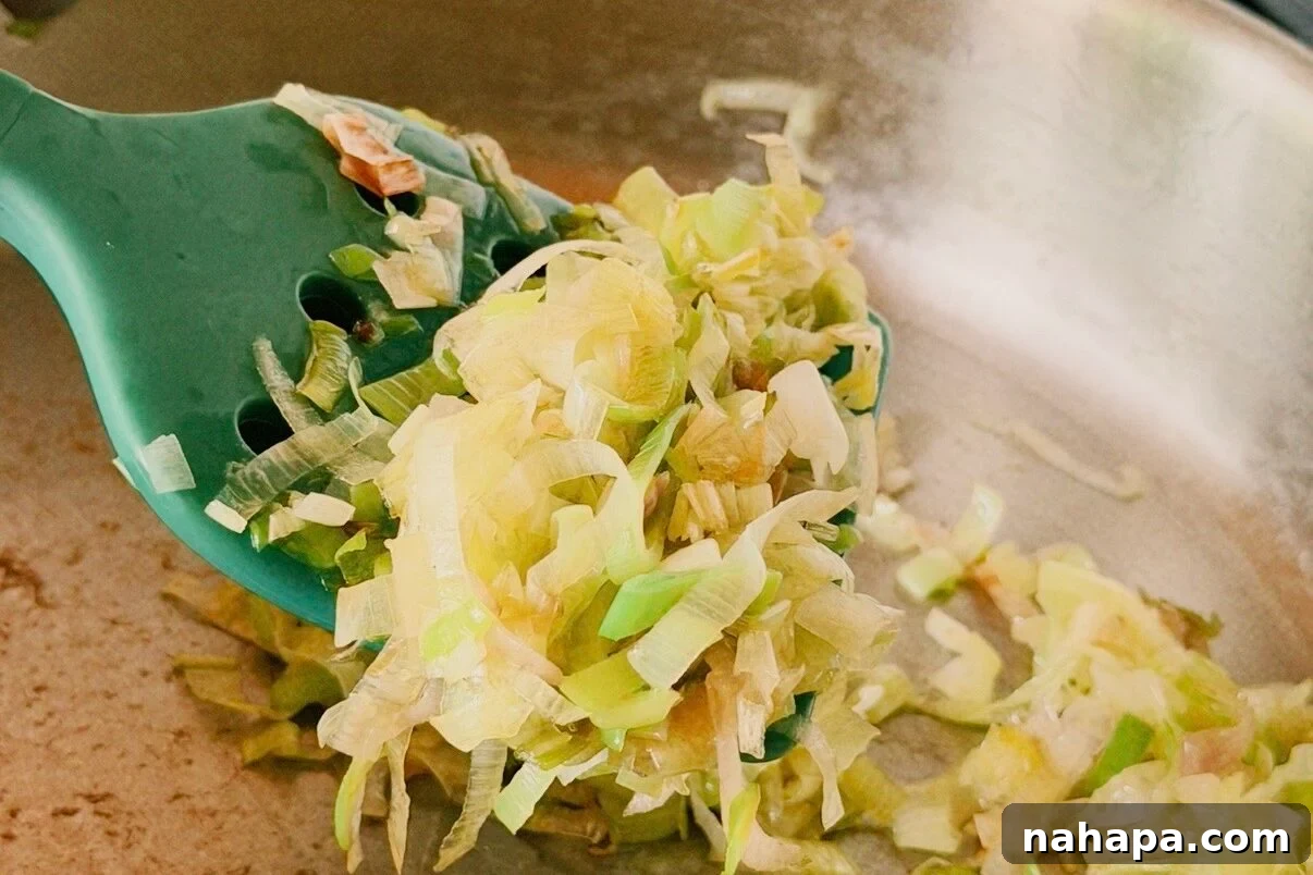 Luscious Dairy-Free Chicken Stuffed Shells 5 A saute pan with leeks and garlic sauting in it with a green spatula.