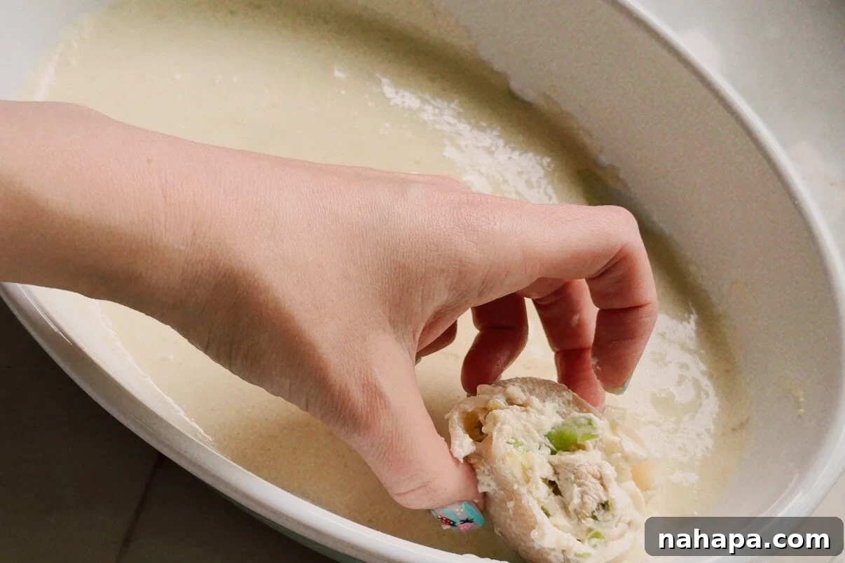 Luscious Dairy-Free Chicken Stuffed Shells 8 A white ceramic dish with a hand putting a stuffed shell in it.