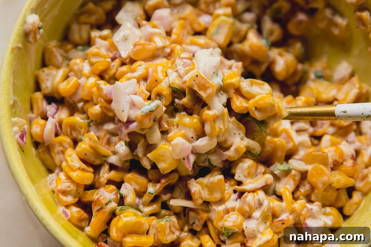 A bowl of creamy street corn mixture, showcasing finely diced red onion, fresh cilantro, and a zesty lime dressing.
