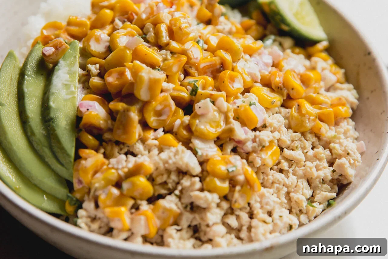 A completed street corn ground chicken bowl, beautifully arranged with fluffy rice, seasoned chicken, creamy street corn, fresh avocado slices, and a vibrant lime wedge, ready to be enjoyed.