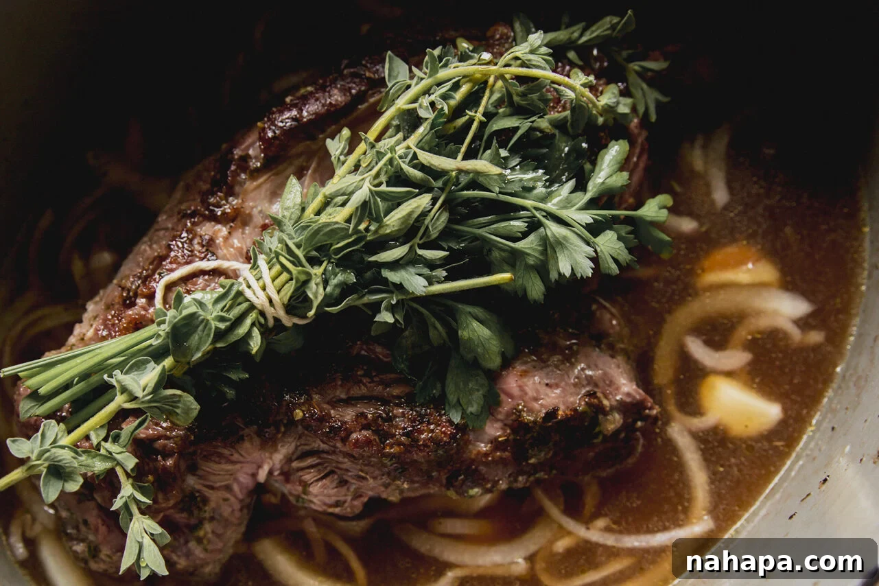 The chuck roast cooking with vinegar and onions, topped with a fresh herb bundle before going in the oven.