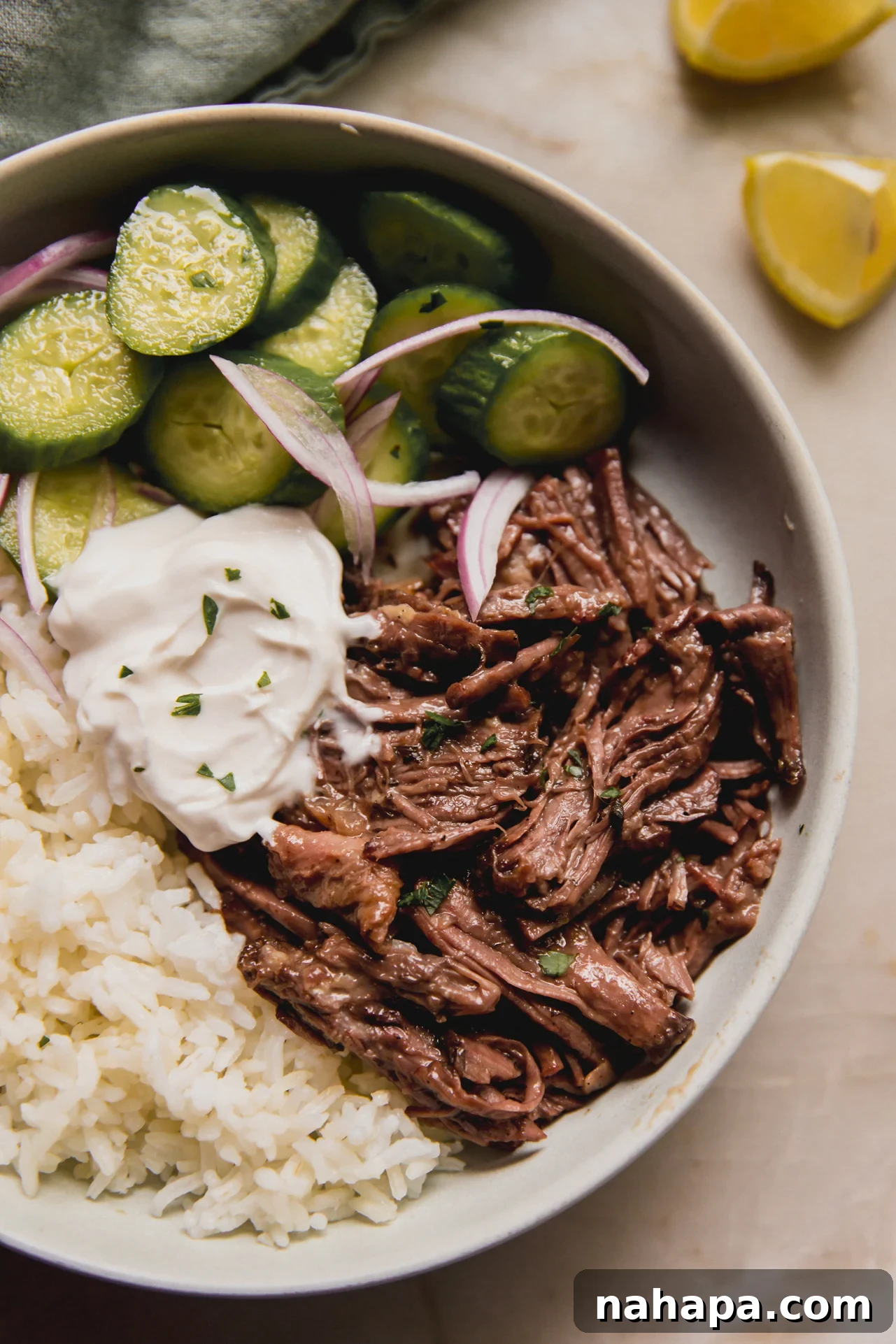 A bowl of Mediterranean pot roast with rice, a dollop of tzatziki, and a side of fresh cucumber salad, ready for serving.