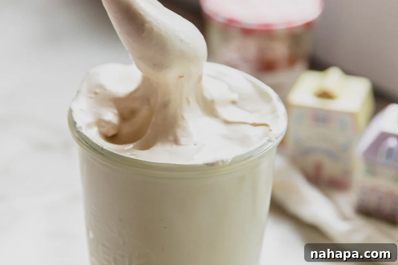 A glass jar filled with peach vanilla marshmallow fluff with a spoon scooping some out.