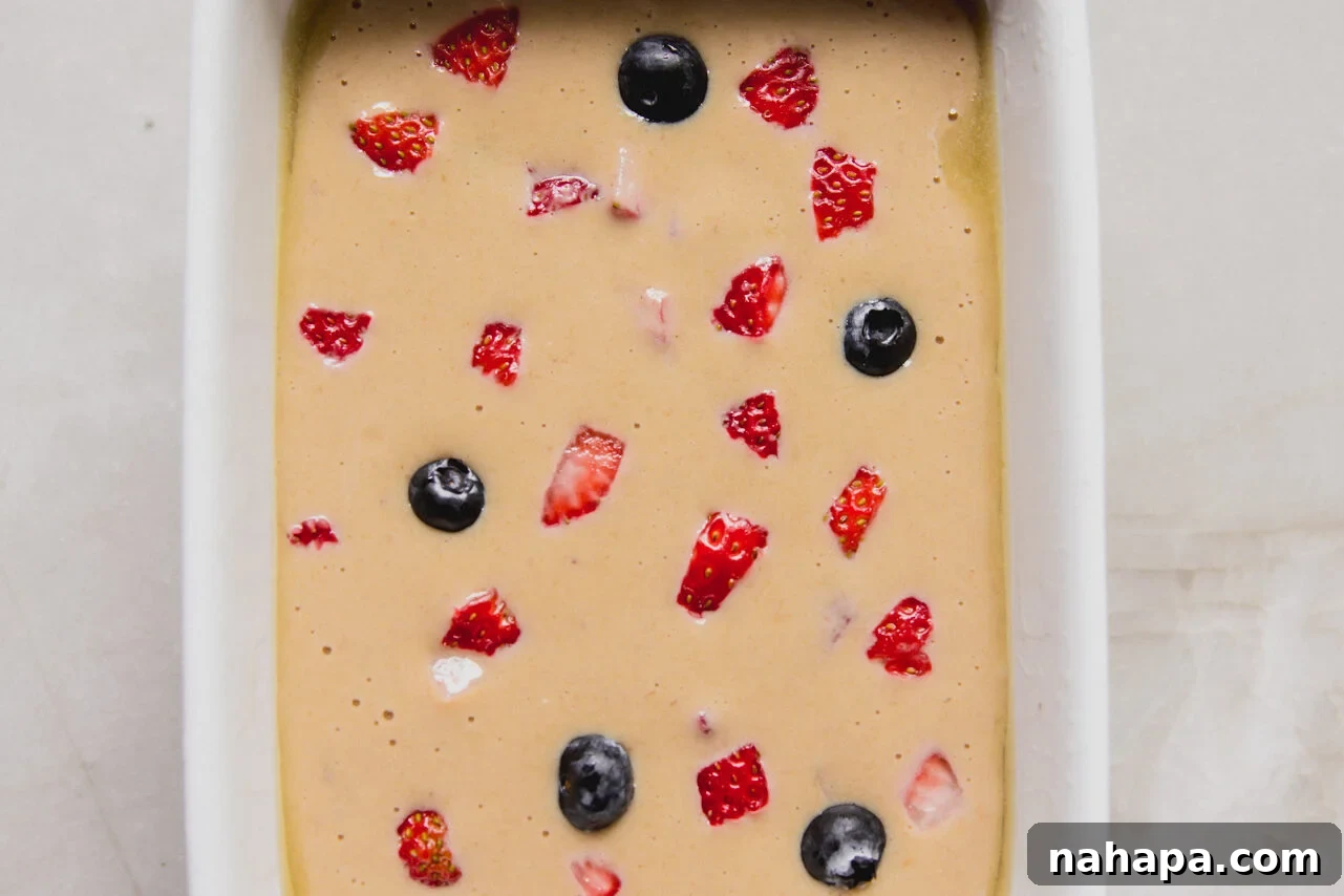The batter for berry protein breakfast cake added to the ceramic baking dish with extra berries on top before baking.