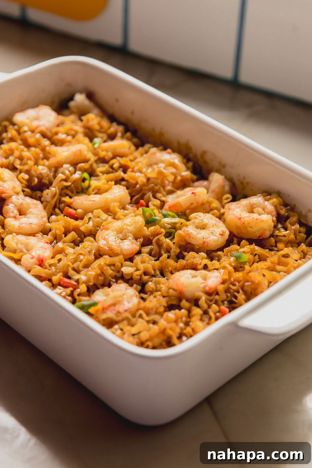 Cooked shrimp and ramen in a large white glass baking dish.