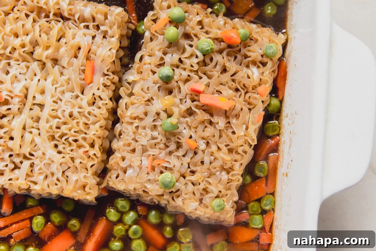 A white casserole dish with mixed vegetable and sauce topped with two ramen bricks.