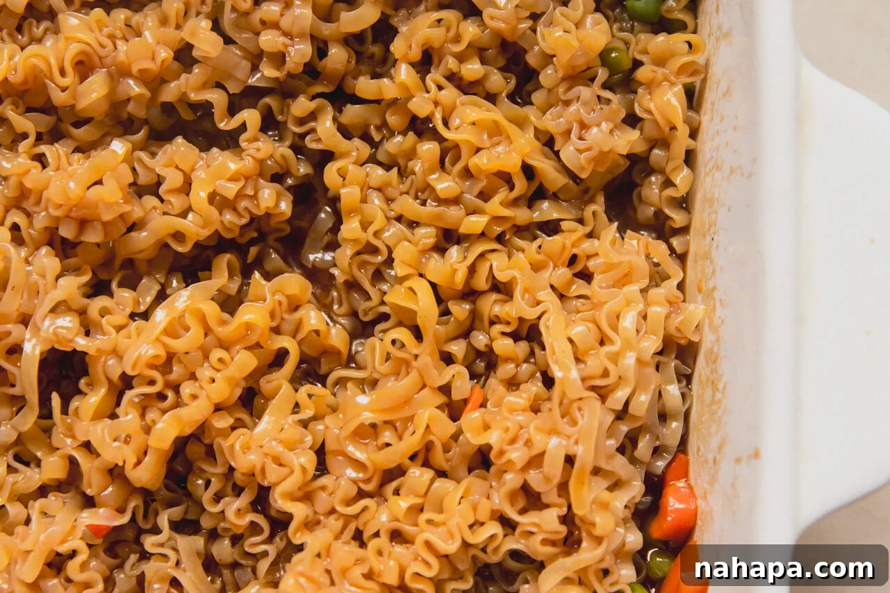 A white casserole dish with mixed vegetable, sauce, and ramen mixed in it.