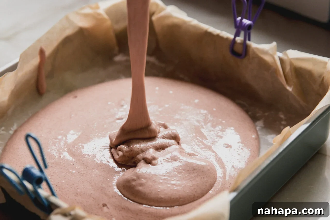 The marshmallow mixture being poured into a pan lined with parchment paper.