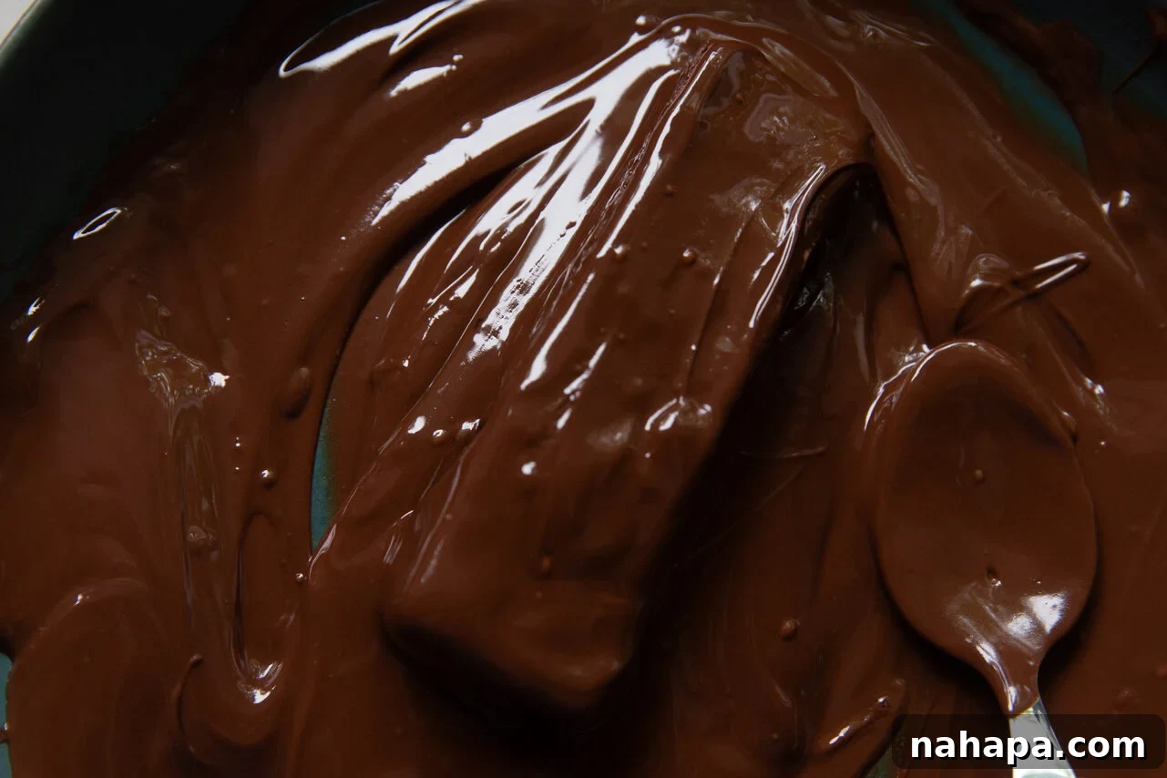 A blue bowl filled with melted chocolate chips and coconut oil that has been mixed with a metal spoon.