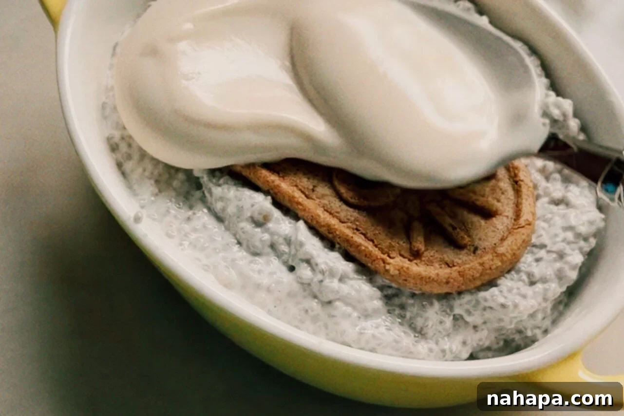 A ramekin filled with chia seed mixture with a breakfast biscuit on top and a spoon adding yogurt over the top.