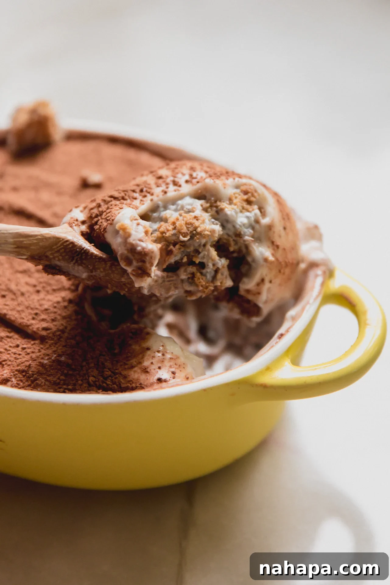 Protein tiramisu in a small yellow dish with a spoon scooping out a scoop.