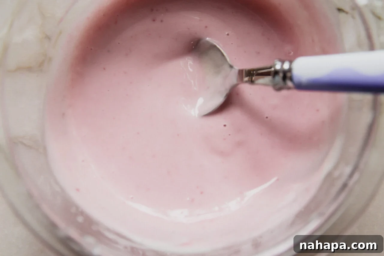 A glass bowl with a yogurt blackberry icing mixture being mixed by a spoon.