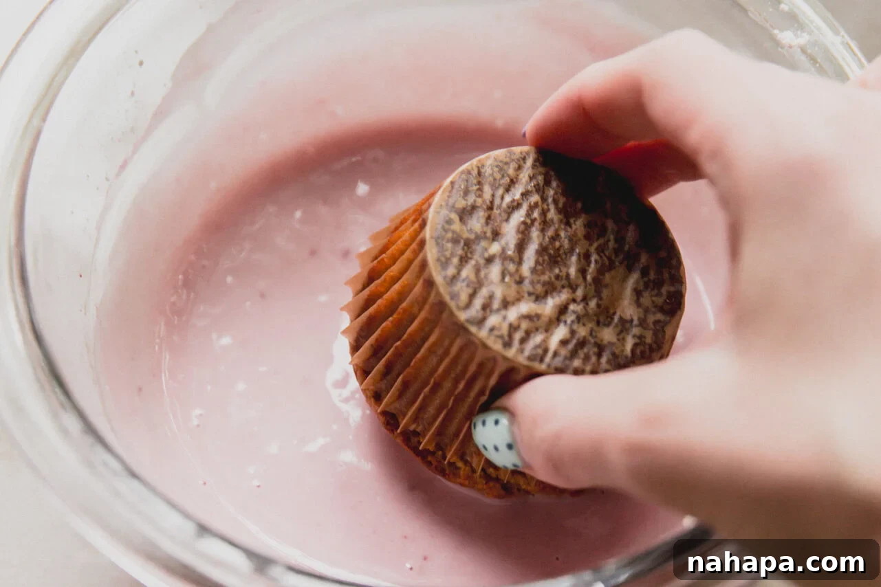 A hand dipping a high protein muffin into the greek yogurt icing in a glass bowl.