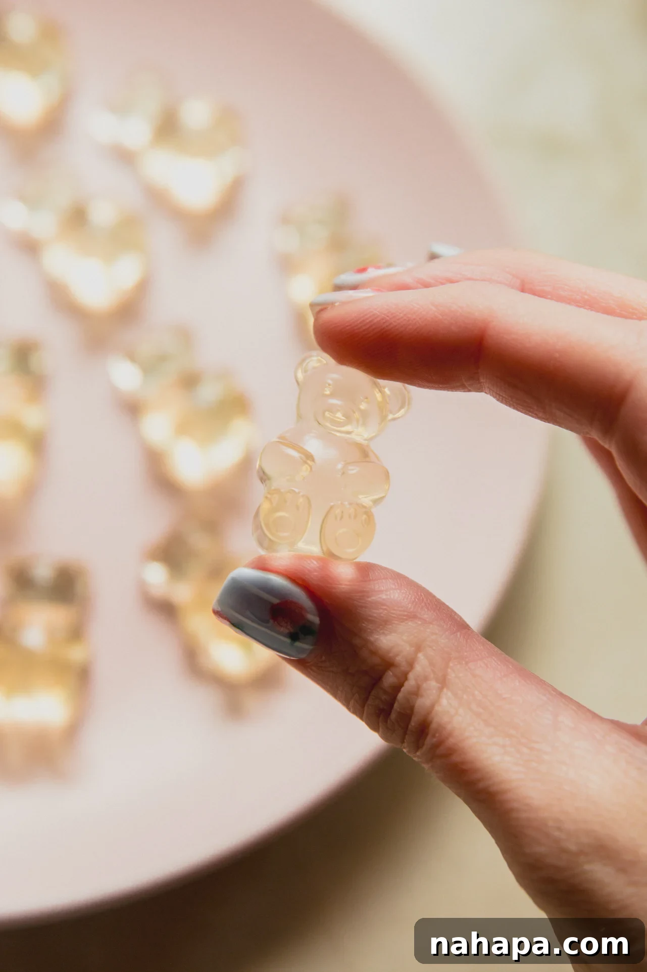 A hand holding a pickle gummy above a plate of pickle gummies.