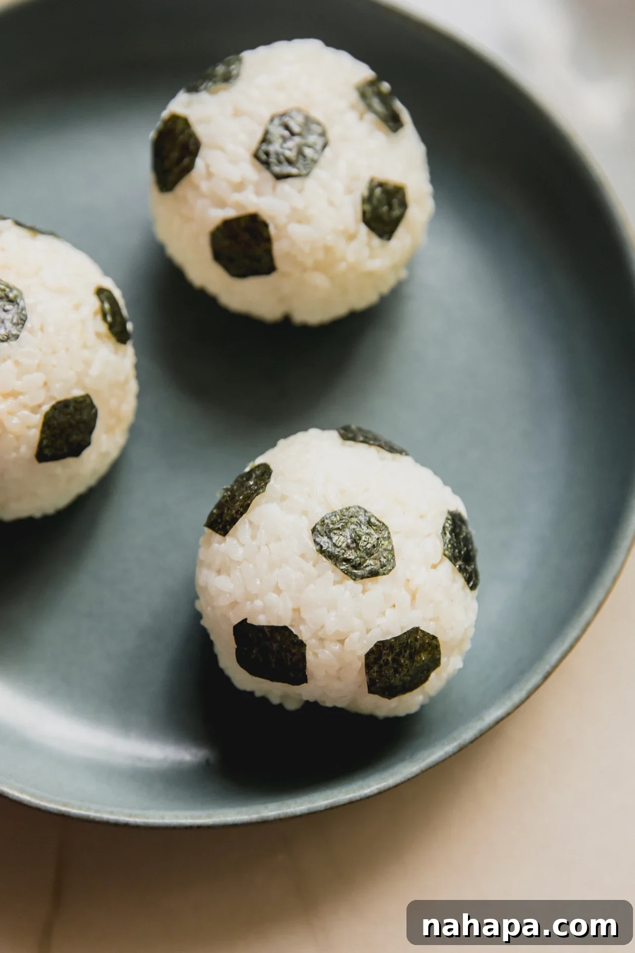 Tuna Onigiri Shaped Like Soccer Balls 2 Three rice balls in a green bowl decorated with seaweed to resemble soccer balls.