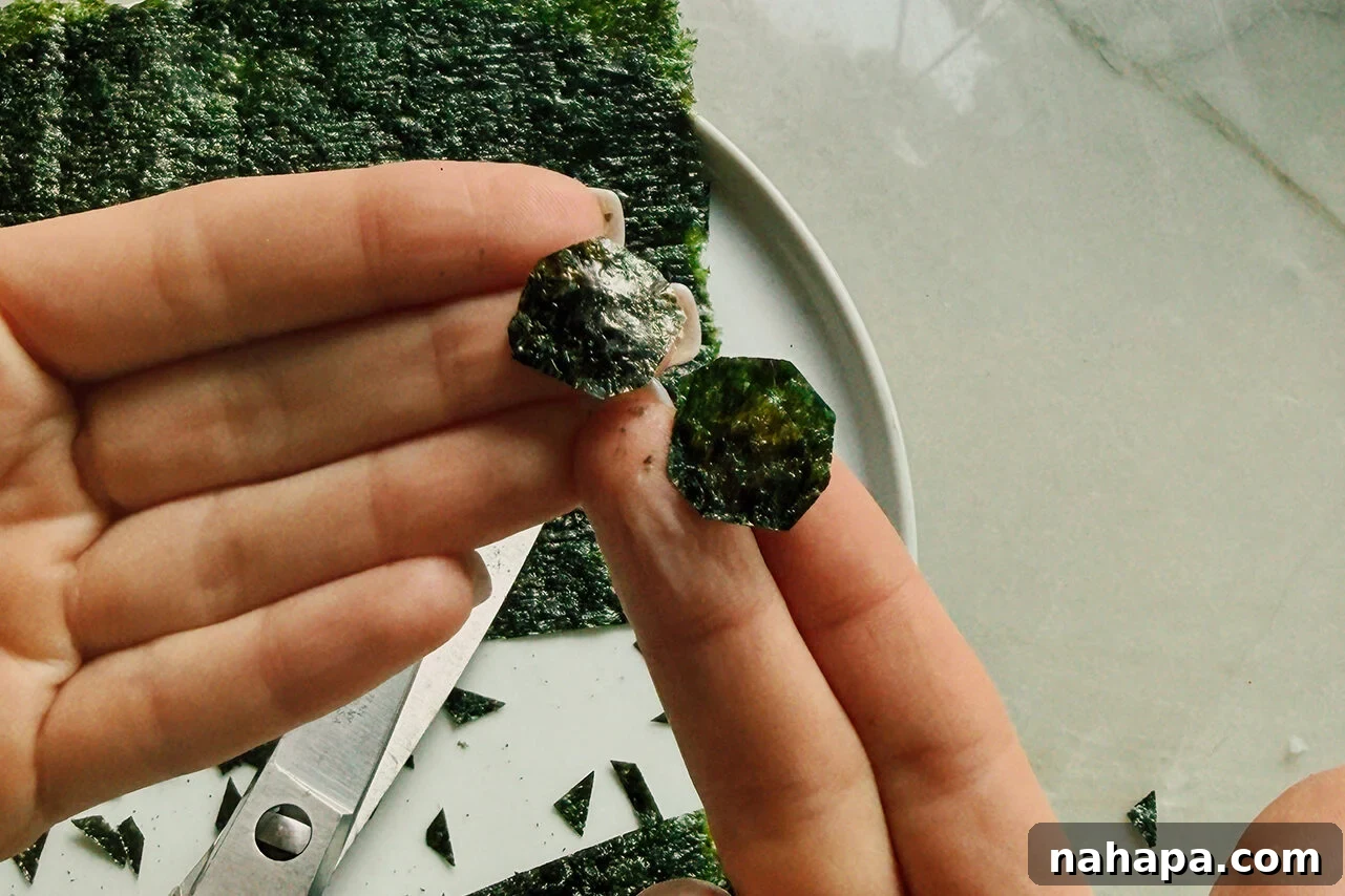 Tuna Onigiri Shaped Like Soccer Balls 7 Seaweed cut into soccer balls being held in a hand above scissors and extra seaweed.