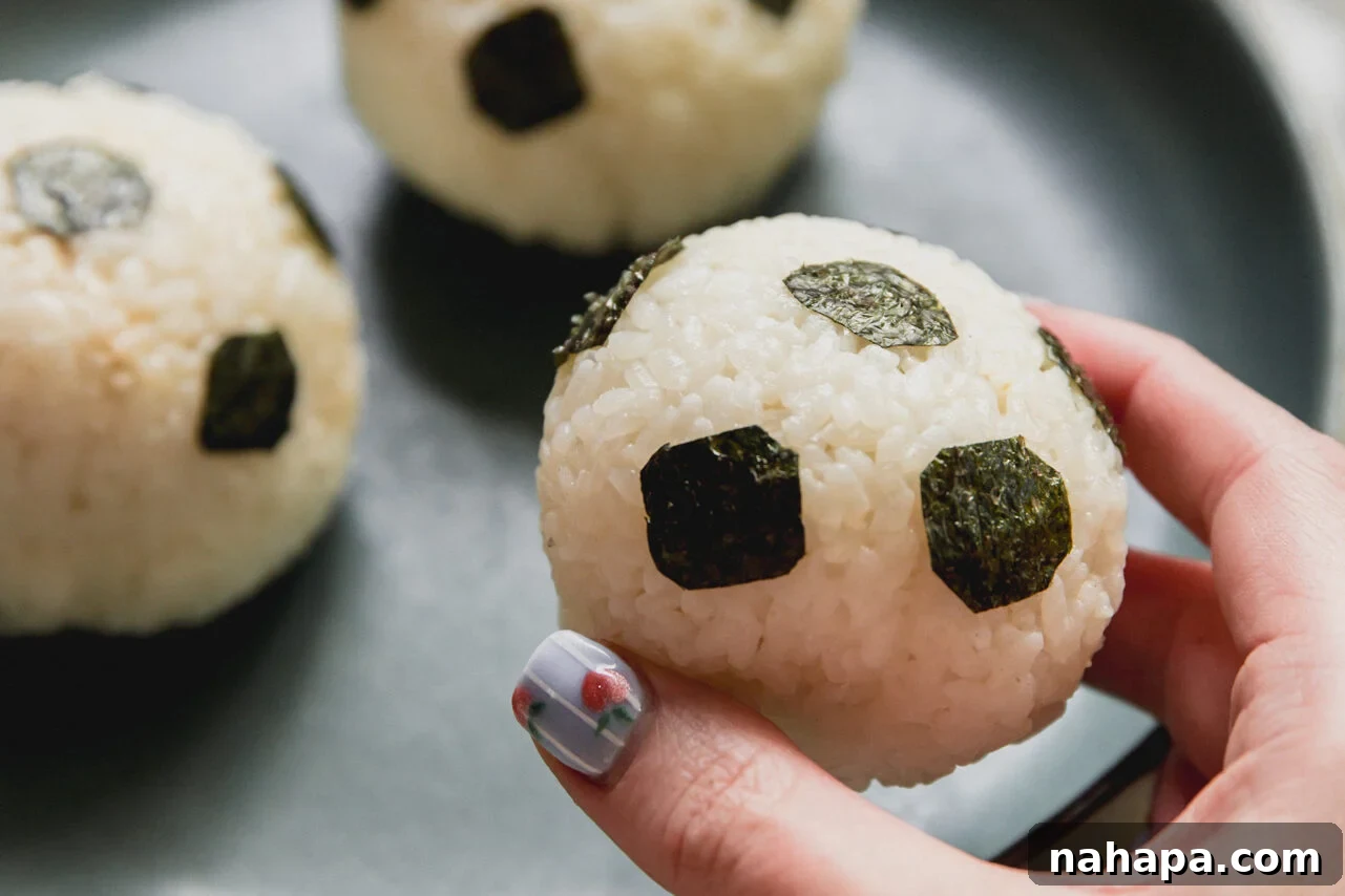 Tuna Onigiri Shaped Like Soccer Balls 8 A plate with soccer tuna rice balls with a hand lifting one of the balls up.