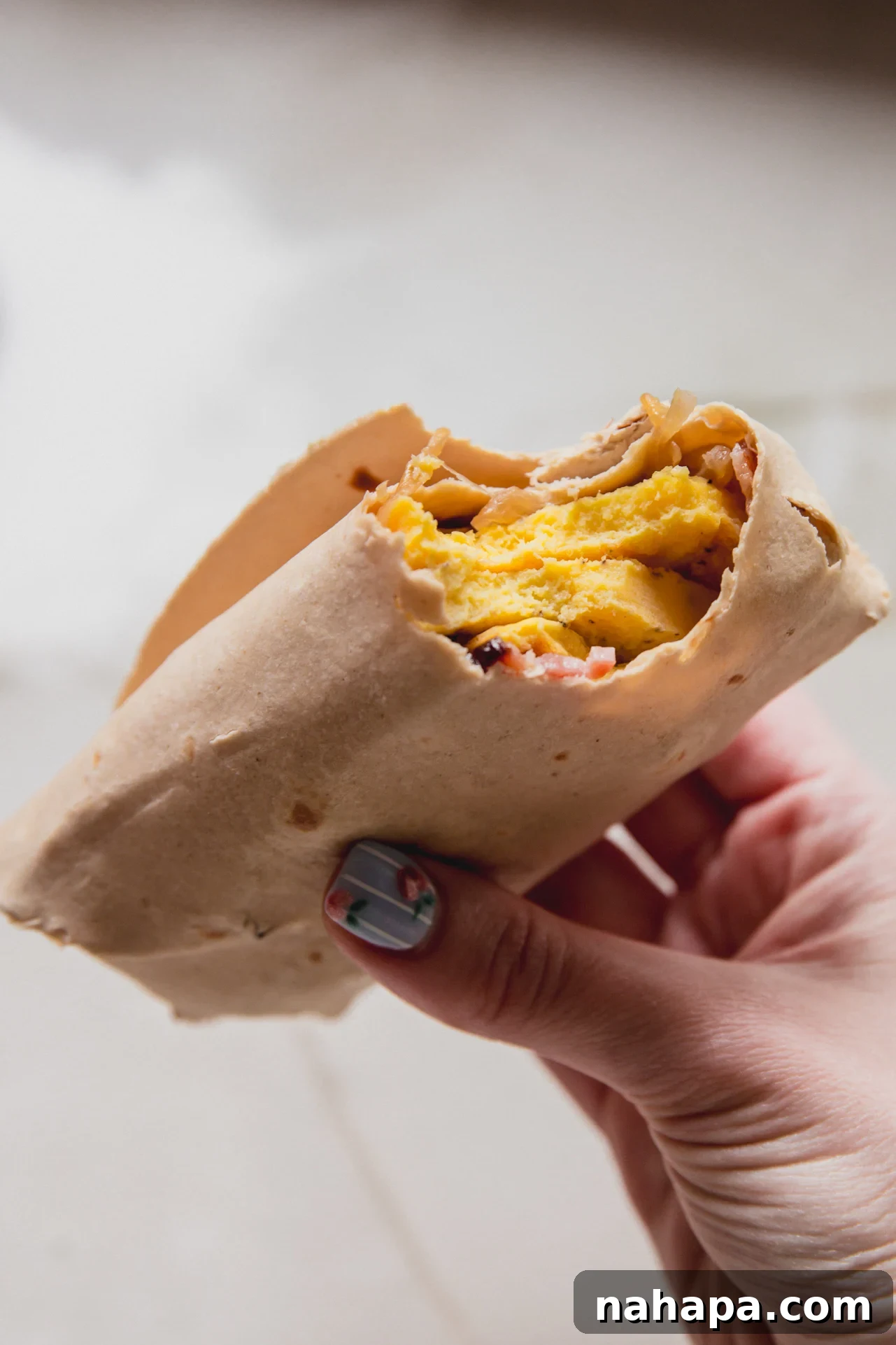 Caramelized Onion Breakfast Burritos with Eggs and Cheese 8 A hand holding a caramelized onion breakfast burrito with a bite taken out of it.