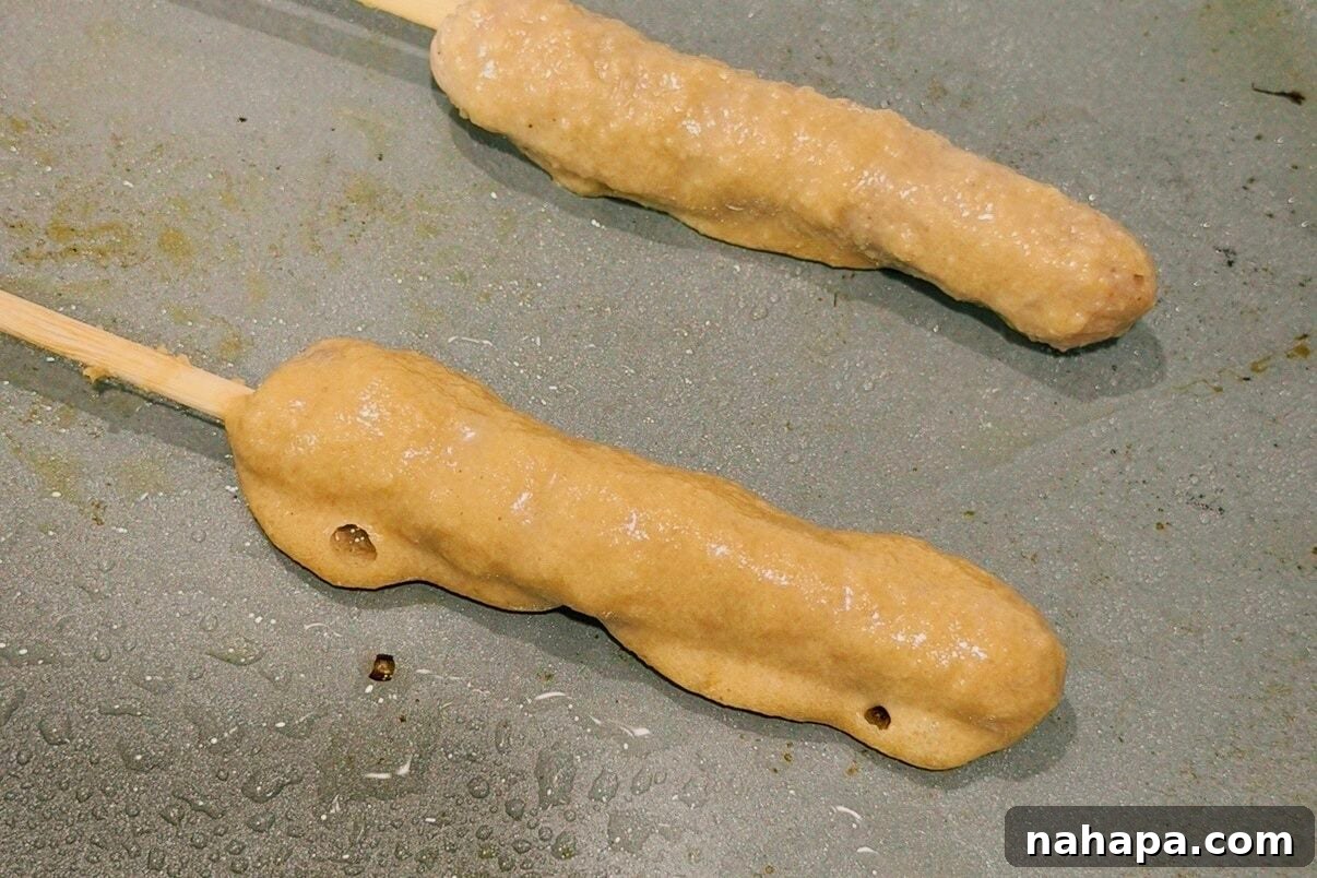 Gluten-Free Pancake and Sausage Sticks Recipe 7 Two chicken sausage pancake skewers cooking on a nonstick pan.