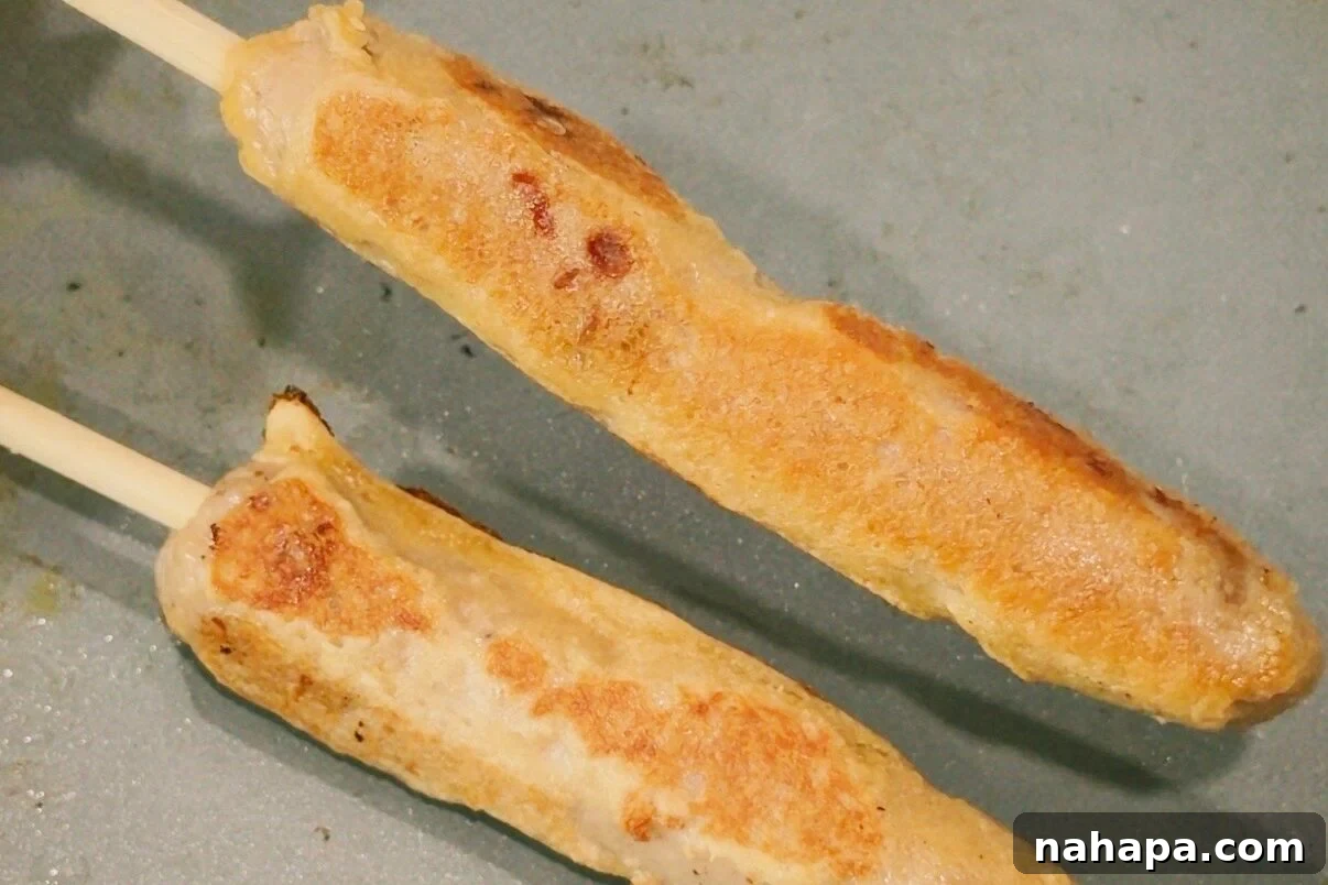 Gluten-Free Pancake and Sausage Sticks Recipe 8 Two chicken sausage pancake skewers cooking on a nonstick pan after turning it.