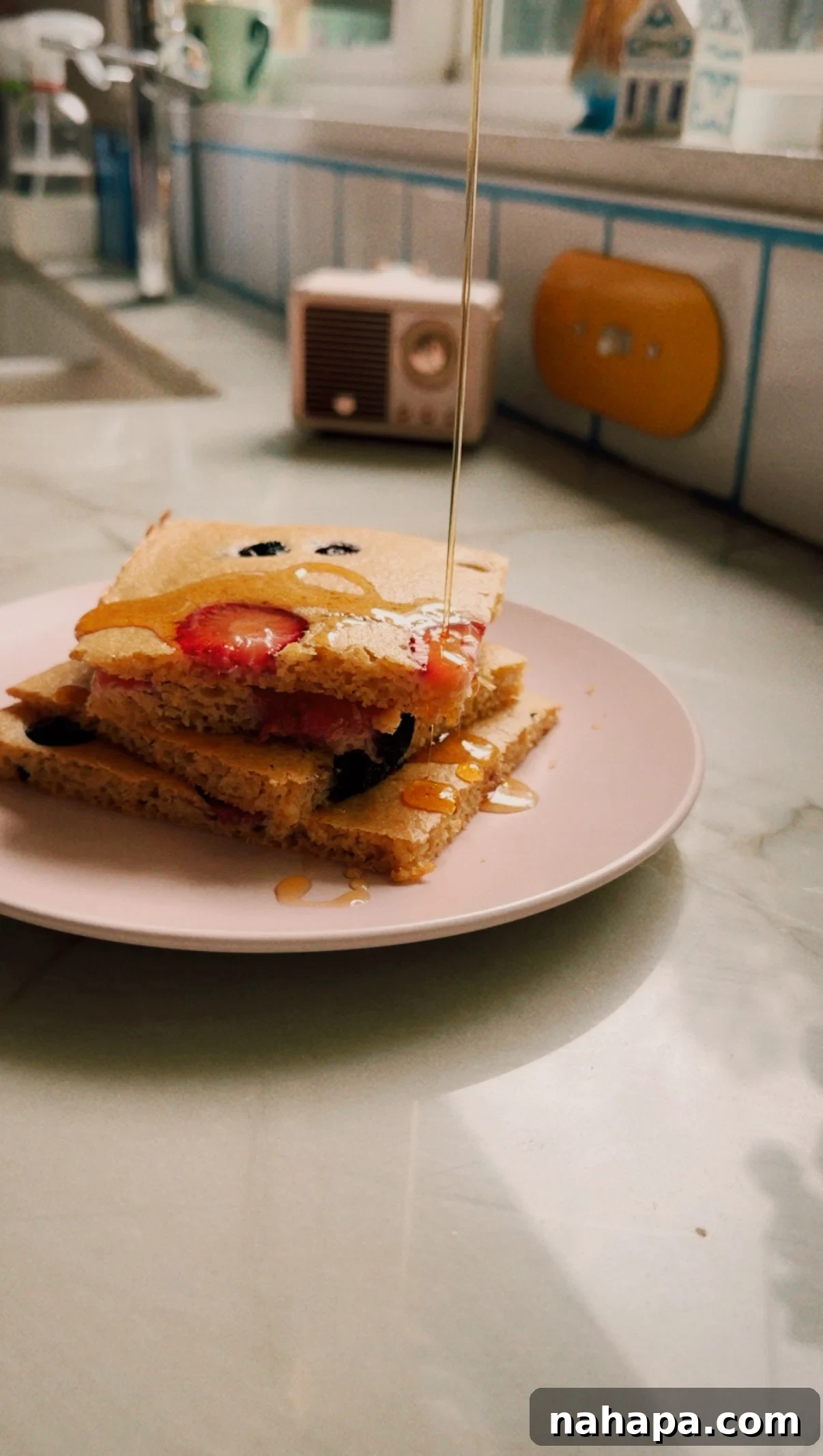 A stack of sheet pan pancakes with maple syrup being poured over