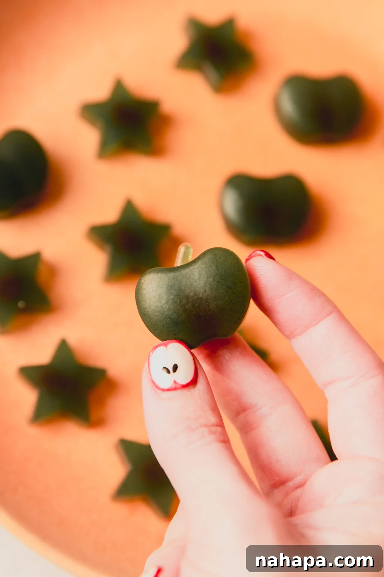 Green apple shaped gummy being held.